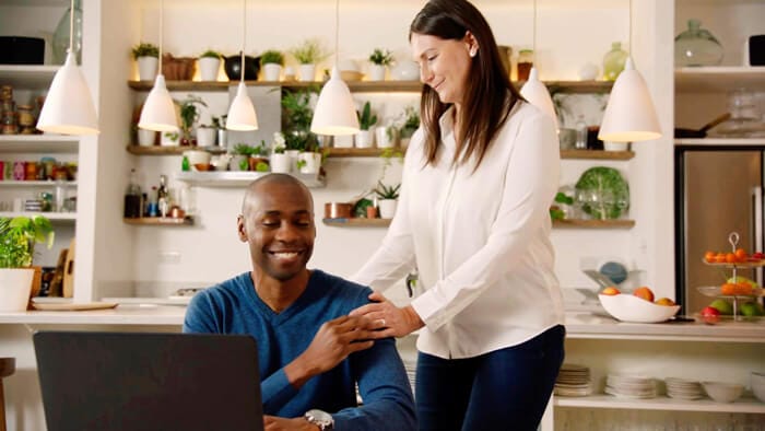 Mies istuu keitti&ouml;ss&auml;. Vaimo seisoo h&auml;nen vieress&auml;&auml;n ja katsoo h&auml;nt&auml; hymyillen.