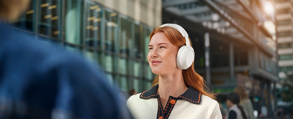 Henkilö käyttää Philips TAH8000EWT over-ear-kuulokkeita ulkona kaupunkimaisemassa