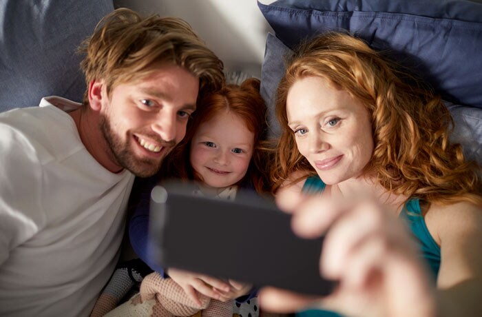 Nainen ottaa selfien yhdessä miehensä ja nuoren tyttärensä kanssa.