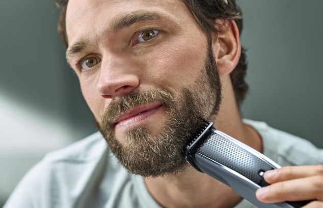 Parrakas, ruskeahiuksinen mies ajaa partaansa sähköisellä partakoneella.