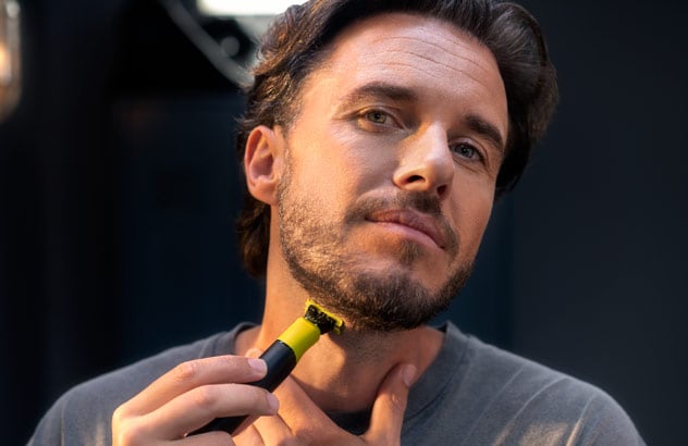 Lähikuva miehestä, joka leikkaa tummaa partaansa Philips OneBlade -partakoneella peilin edessä.