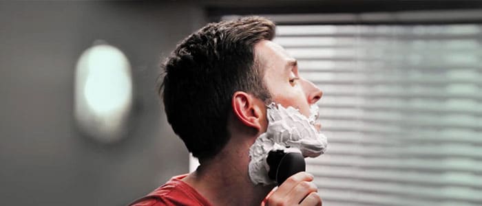 Mies, jolla on partavaahtoa kasvoillaan, ajelee partaansa partakoneella.